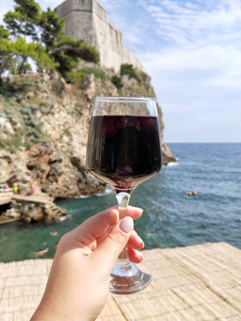 hand holding red wine glass in front of sea and cliff background