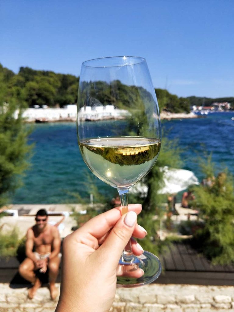 hand holding white wine in glass with sea background in the sun