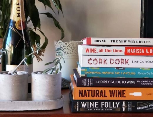 best wine books 2020 stacked up on wooden TV cabinet next to succulent plants and moet wine bottle