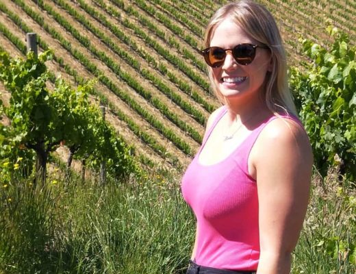 blonde woman in pink top standing in basket range vineyard