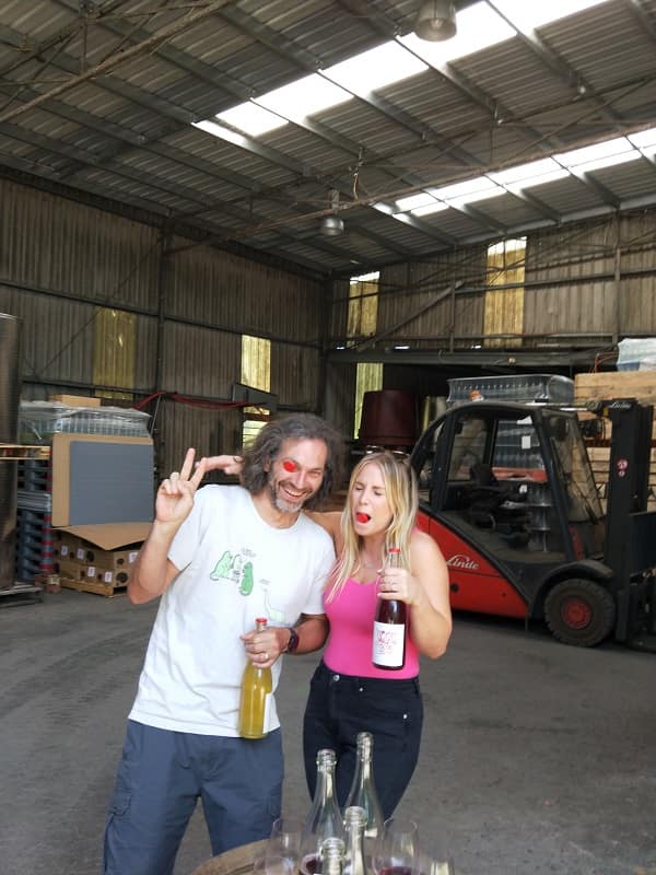 the other right winemaker alex schulkin holding wine with a bottle top in his eye posing with blogger holding wine