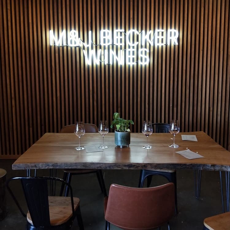 M&J Becker light sign above wooden table with wine glasses on at one of Hunter Valley organic wineries