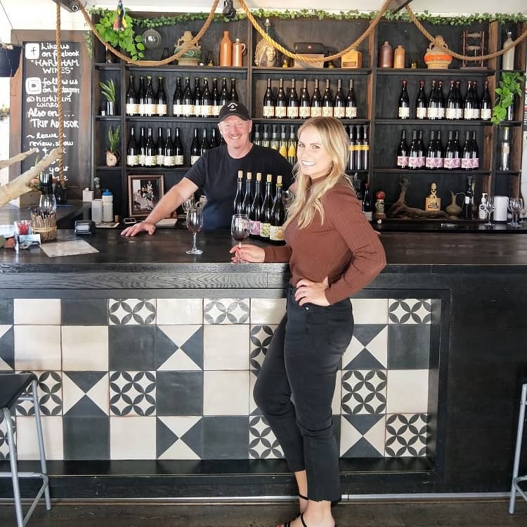 Blonde woman standing in front of bar with man serving Harkham wines