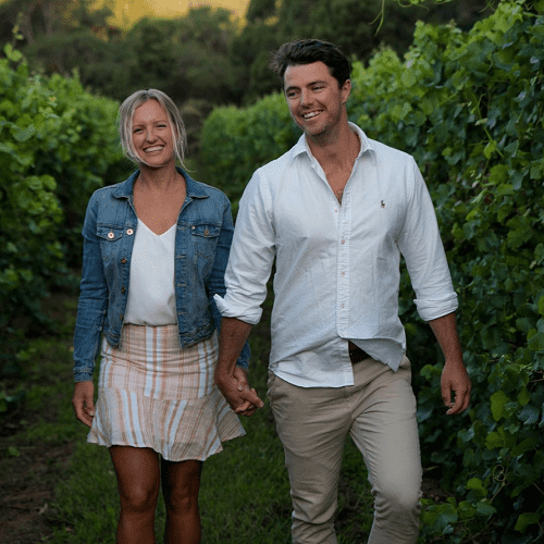 blonde woman and brown haired man holding hands in vineyard 