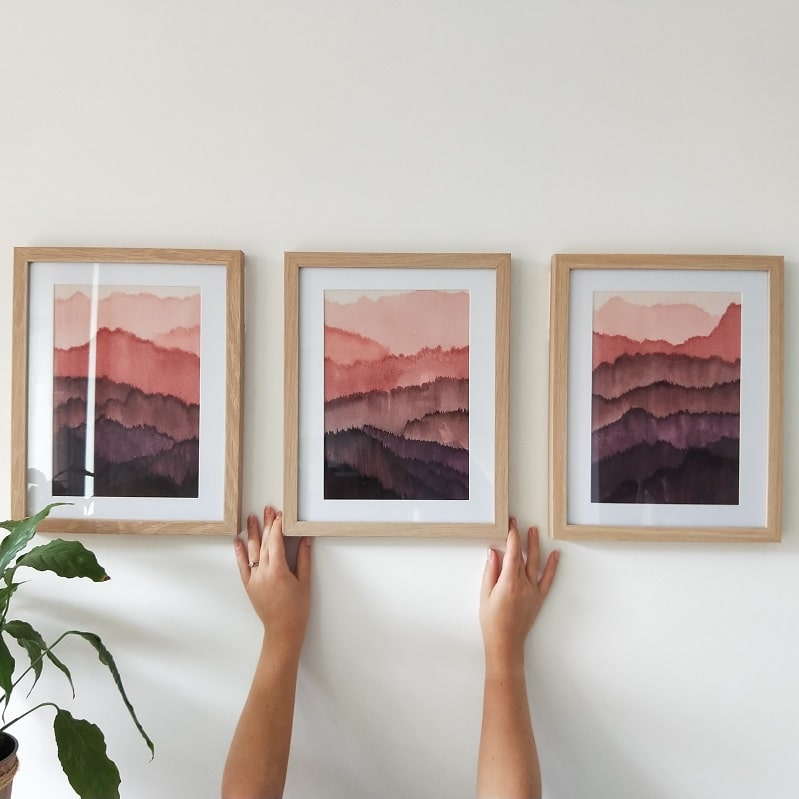 christmas gift guide hands holding up three wine paintings of mountains in purple and pink