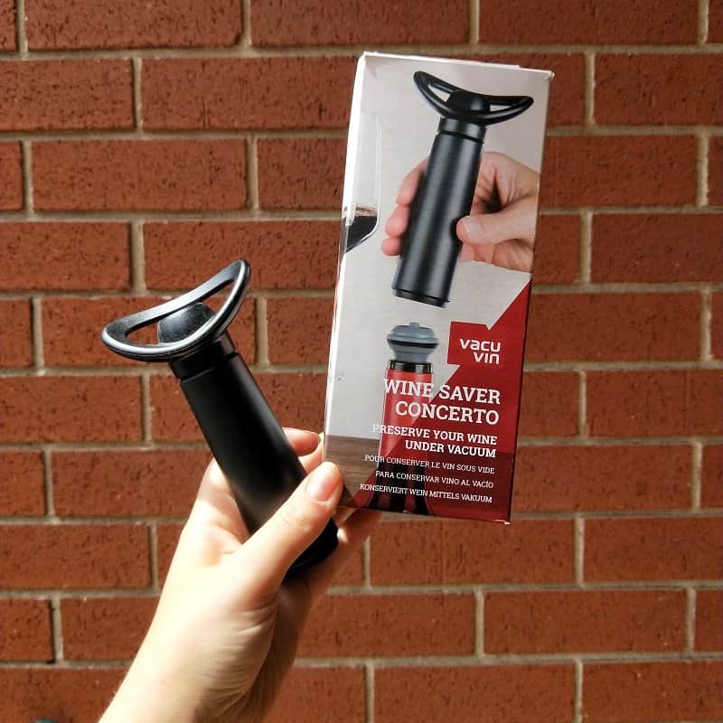 Christmas gift guide hand holding vacuvin in front of brick wall